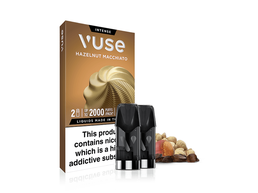 A Vuse Hazelnut Macchiato vape pod pack with two vape pods in front and a mix of hazelnuts, coffee beans, and macchiato swirl behind. The packaging displays nicotine and warning information.
