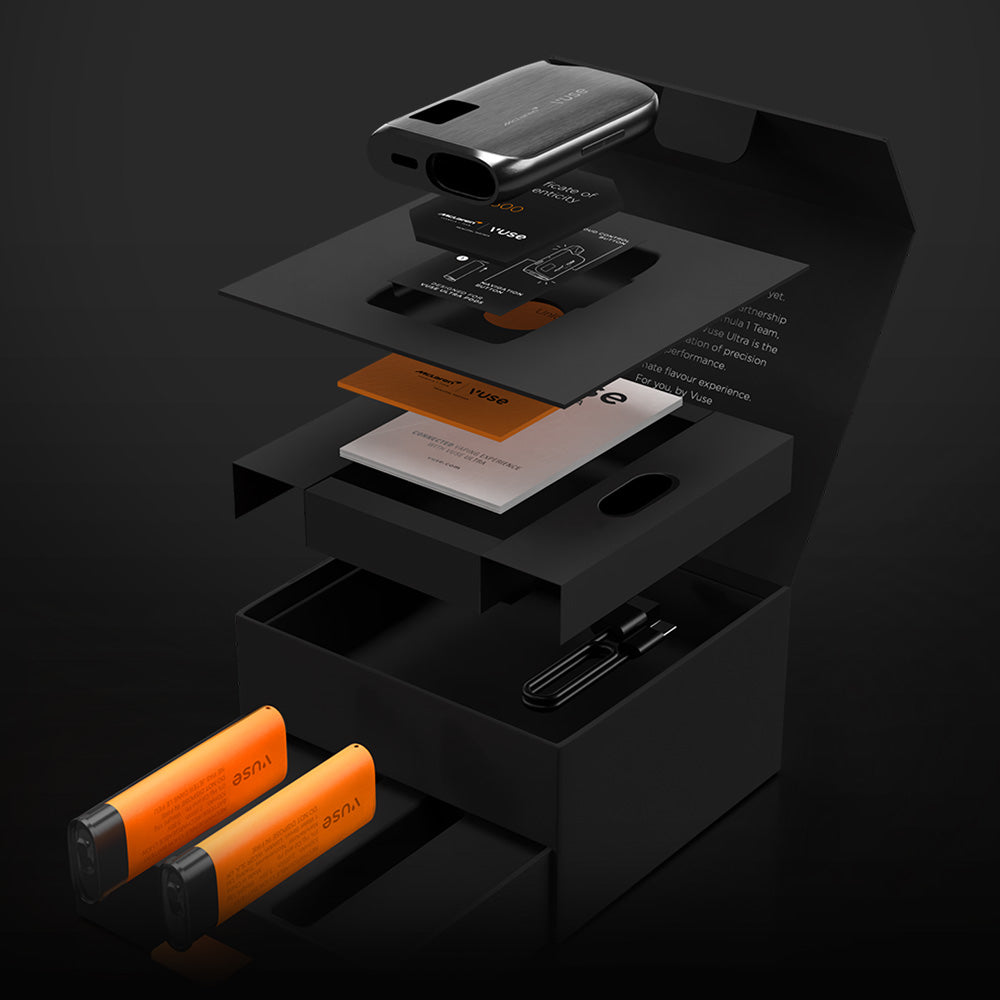 An exploded view of a sleek black box containing a vape device kit, including the device, instruction cards, USB cable, and two orange vape pods, all neatly organized in separate compartments.