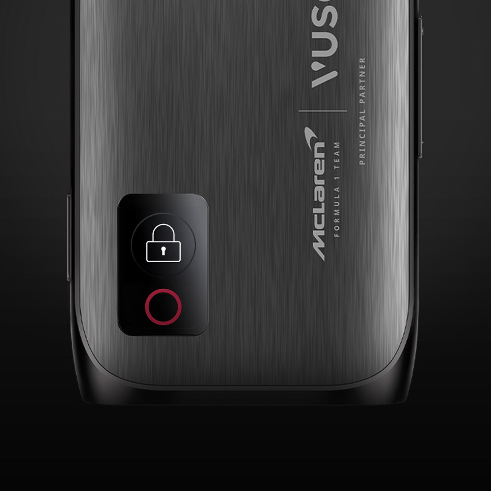 Close-up of a metallic device with a brushed finish, featuring a button with a lock icon and a red circle. The device displays McLaren and Vuse branding on its surface.